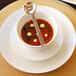 A bowl of soup with a spoon in it on a white porcelain plate.