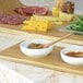 A wooden tray with a Front of the House Harmony bright white porcelain ramekin of food on it.