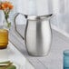 A silver stainless steel Vollrath bell pitcher on a table.