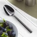 An Acopa Phoenix stainless steel teaspoon next to a bowl of fruit.