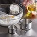 A person using a Vollrath stainless steel measuring cup to pour flour into a bowl.