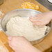 A person's hand kneading pizza dough in a bowl.