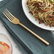 An Acopa Phoenix stainless steel dinner fork next to a plate of spaghetti and mushrooms.