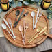 A wooden cutting board with Acopa Phoenix stainless steel forks and candles on a table.