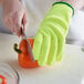 A person wearing yellow Mercer Culinary Millennia kitchen gloves cutting a bell pepper with a knife.