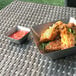 A metal container of sauce on a table with a Front of the House stainless steel ramekin full of red sauce.