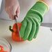 A person wearing Mercer Culinary Millennia Colors green gloves cutting a pepper with a knife.