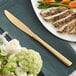 An Acopa Phoenix stainless steel dinner knife on a napkin next to a plate of food.