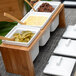 A white square porcelain pot with a notched lid on a wooden tray with bowls of sauces and pickles.