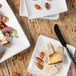 A Front of the House bright white square porcelain plate with food including cheese and crackers on it.
