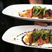 Two Front of the House rectangular white porcelain platters with food on a table.
