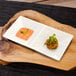 A wood tray with a rectangular white porcelain plate holding two small rectangular white porcelain sauce dishes.