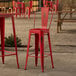 A red metal Lancaster Table & Seating outdoor cafe barstool at a table with beer glasses on it.