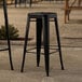 A pair of Lancaster Table & Seating black metal outdoor barstools on a stone surface.