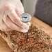 A dial probe thermometer being used to measure the temperature of a seasoned meat roast.