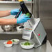 A person wearing blue gloves uses a Hobart food processor to cut green peppers.