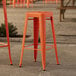 A Lancaster Table & Seating orange metal outdoor barstool.