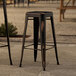 Two Lancaster Table & Seating distressed copper outdoor barstools on a stone patio.