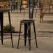 A black Lancaster Table & Seating outdoor cafe barstool at a table with drinks on an outdoor patio.