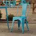 A turquoise Lancaster Table & Seating outdoor cafe chair on a stone patio.