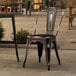 A Lancaster Table & Seating black metal outdoor cafe chair sits at a table on a patio.