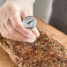 A pocket probe dial thermometer being used to check the temperature of a seasoned meat roast.
