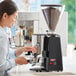 A woman using an Estella Caffe espresso grinder on a counter in a professional kitchen.