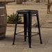 A Lancaster Table & Seating black metal backless counter height stool on a stone surface.