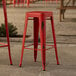 A red Lancaster Table & Seating outdoor backless barstool on a stone patio.