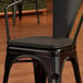 A black Lancaster Table & Seating chair with a wooden seat.