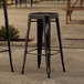 Two Lancaster Table & Seating black metal backless barstools on a stone surface.