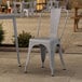 A Lancaster Table & Seating gray metal outdoor cafe chair on a stone patio.