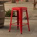 A red Lancaster Table & Seating outdoor backless counter height stool on a stone patio.