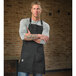 A man wearing a Mercer Culinary black canvas bib apron with black leather straps.