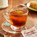 A glass cup of Bigelow Eggnogg'n tea on a saucer with a tea bag in it.
