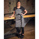 A woman wearing a gray Mercer Culinary Odin Bib Apron with black webbing.