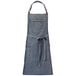 A grey denim Mercer Culinary bib apron with brown leather straps and a tie.