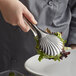 A person using Vollrath stainless steel scalloped serving tongs to serve salad.