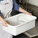A woman in an apron holding a white Tablecraft bus tub full of dishes.