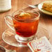 A glass cup of Bigelow Salted Caramel tea with a tea bag on a saucer.