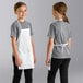 A girl wearing a white Uncommon Chef child bib apron with 2 pockets and smiling.