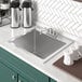 A Regency stainless steel drop-in sink with a white coffee mug and containers on the counter above.