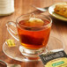 A glass cup of tea with a Bigelow French Vanilla Decaffeinated Tea bag on a saucer.