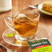 A glass cup of Bigelow Green Tea with a tea bag on a saucer.