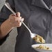 A person using a Vollrath stainless steel serving spoon to serve food from a bowl.