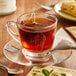 A glass cup of Steep Cafe By Bigelow Organic South Indian Select Black Tea with a tea bag on a saucer and a spoon.