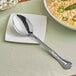 A Vollrath stainless steel serving spoon on a white plate with food.