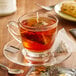 A glass cup of Steep Cafe By Bigelow Organic Chai Black Tea with a tea bag on a saucer.