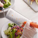 A gloved hand using a Mercer Culinary stainless steel coarse grater to grate a carrot.