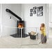 A child standing in front of a fireplace using a white BabyDan safety gate.